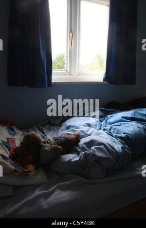 Kinderzimmer mit offenen Vorhängen und ein Plüschtier auf der Bettdecke. Stockfoto