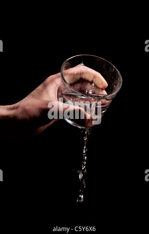 Männer Hand goss Wasser aus einem Glas auf einem schwarzen Hintergrund Stockfoto