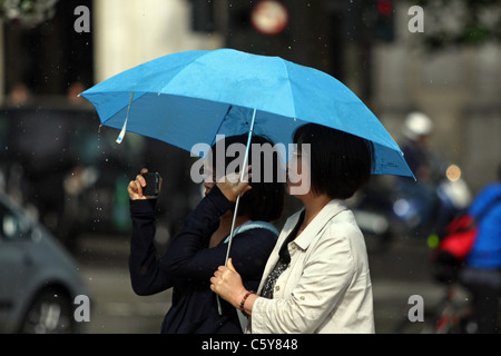 Zwei Damen Zuflucht vor dem Regen unter ihren Sonnenschirmen und ein Foto, in London. Stockfoto