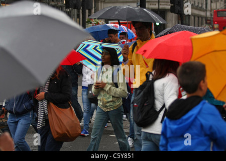 Menschen, die Zuflucht vor dem Regen unter ihren Sonnenschirmen in London. Stockfoto