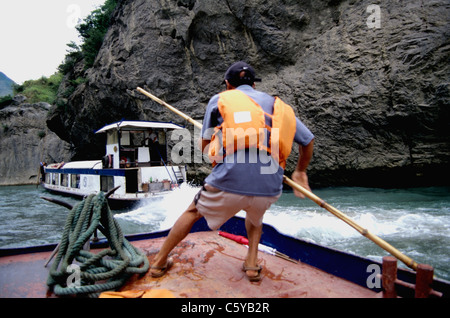 Bootsmann mit langen Bambusstab führt Ausflugsboot auf Nebenfluss Daning Jangtse. Stockfoto