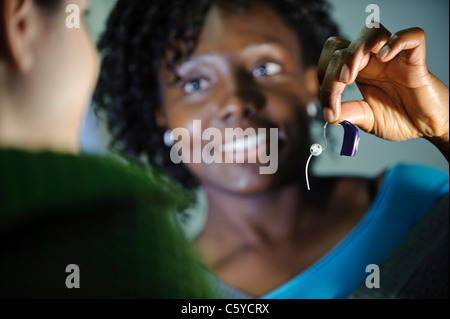 Audiologie und Taubheit Studentin hält ein kleines Hörgerät zu einem anderen Audiologie Studenten zeigen Stockfoto
