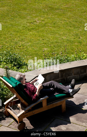 Entspannen Sie sich auf Chaise Lounge Chair auf Steinplatten Deck reifer Mann Stockfoto