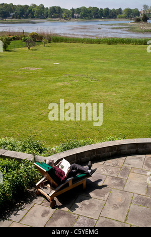 Reifen Sie Mann, entspannend, Lesung Magazin auf Chaise Lounge Stuhl auf Steinplatten Terrasse im Hinterhof Stockfoto