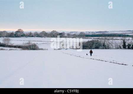 Ein Mann geht seinen Hund durch ein Schneefeld bedeckt. Stockfoto