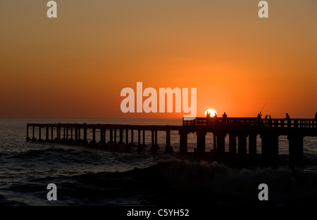 Fischer und Touristen beobachten den Sonnenuntergang über dem Ozean von der Seebrücke entfernt. Swakopmund, Namibia. Stockfoto