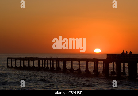 Touristen beobachten den Sonnenuntergang über dem Ozean von der Seebrücke entfernt. Swakopmund, Namibia. Stockfoto
