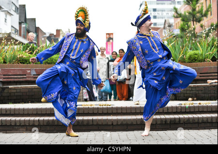 Zwei Bhangra-Tänzer in traditionellen bunten und dekorativen Indianer Kostüm in West Bromwich High Street von einer Menschenmenge beobachtet Stockfoto