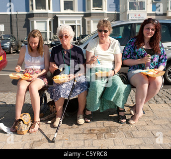 Vier Frauen Essen Fish &amp; Chips sitzen auf einer Bank an der Aberystwyth Ceredigion Wales UK Stockfoto