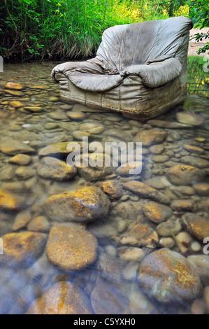 Fliegen Sie kippen. Ein alten Sessel entsorgt illegal in klaren Waldbach. Stockfoto