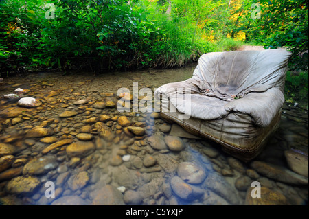 Fliegen Sie kippen. Ein alten Sessel entsorgt illegal in klaren Waldbach. Stockfoto