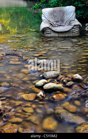 Fliegen Sie kippen. Ein alten Sessel entsorgt illegal in klaren Waldbach. Stockfoto