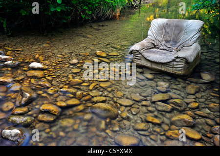 Fliegen Sie kippen. Ein alten Sessel entsorgt illegal in klaren Waldbach. Stockfoto