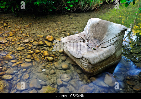 Fliegen Sie kippen. Ein alten Sessel entsorgt illegal in klaren Waldbach. Stockfoto