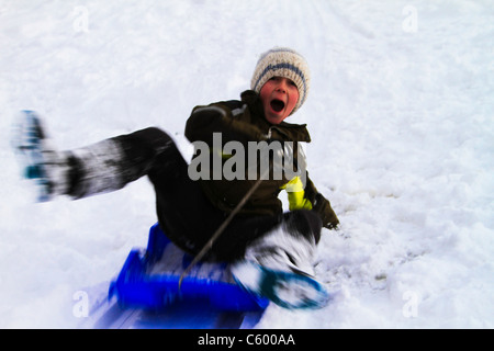 Kleiner Junge (8 Jahre), Schlittenfahren im Schnee mit einem Lächeln auf seinem Gesicht Stockfoto