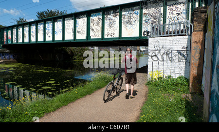 Ein Mann mit seinem Fahrrad auf ein Handy und gehen unter einer Brücke an der Lea Valley Walk Lee Navigation Fluss East London UK KATHY DEWITT Stockfoto