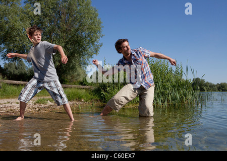 Vater und Sohn überspringen Felsen am See Stockfoto