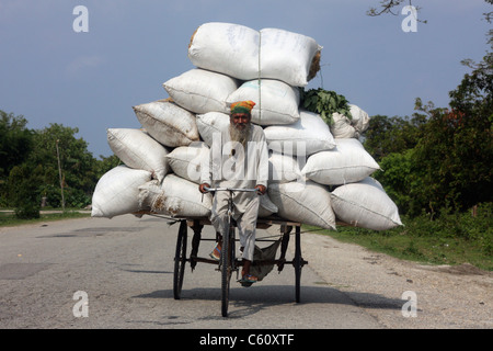 Ältere Nepali Mann fährt Dreirad-Rikscha mit Reis in der Mittagssonne in der Nähe von Damak auf der Südautobahn Nepal overladed Stockfoto