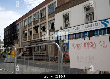 Einige Geschäfte versuchen, zur Normalität zurückzukehren, während andere haben abgerissen werden nach wird in den Aufständen von Woolwich, London brannte Stockfoto