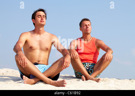Vier junge Menschen auf Sand sitzen und meditieren Stockfoto