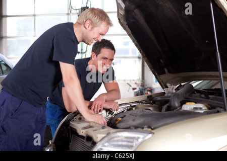 Zwei Mann Mechanik lächelnd und arbeitet unter der Motorhaube eines Autos, geringe Schärfentiefe, scharfen Fokus auf hinteren Mechaniker Stockfoto