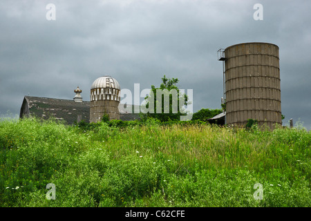 Ländliche Landschaft von Minnesota. Altes Bauernhaus, Scheune und Silo vor dramatischem Himmel im Hintergrund horizontale Hi-res Stockfoto