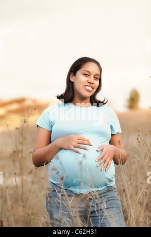 Gerne latino schwangere Frau, Zuneigung zu zeigen Ihr ungeborenes Baby, indem Sie die Hände auf ihren Bauch, auf einem Feld in Kalifornien stehen bei einem Sonnenuntergang Stockfoto