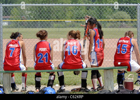 High-School-Mädchen sitzen auf der Bank während einer Auszeit an einem Softballspiel Stockfoto