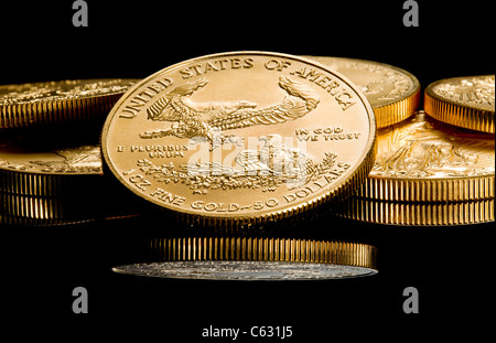 Nahaufnahme einer solid gold Eagle 1 Unze Münze auf anderen Münzen gestapelt und spiegelt sich in schwarze Oberfläche Stockfoto