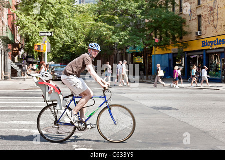 Radfahrer mit Kleinkind im Kindersitz kreuzt eine Kreuzung an der Ninth Avenue in Hells Kitchen Nachbarschaft New York City Stockfoto