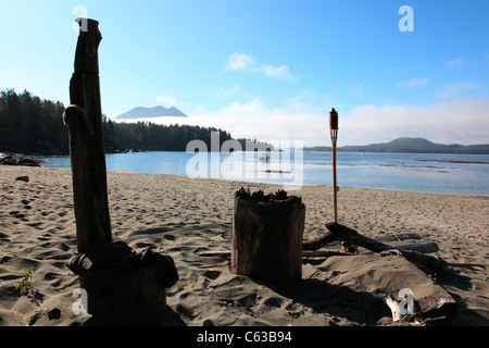 Log und Tiki-Fackel um eine Feuerstelle auf einem sandigen Strand an einem Sommertag in der Nähe von Tofino BC Kanada Stockfoto