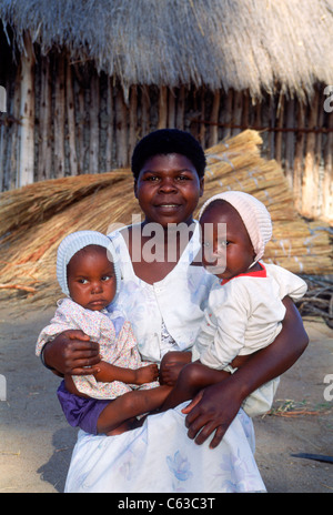 Afrikanerin mit zwei Babys im Arm vor Dorf Hütte in ländlichen Simbabwe Stockfoto