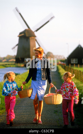 Mutter mit zwei Töchtern und Körbe entlang nach Hause in den Niederlanden Kanal mit Windmühle Stockfoto