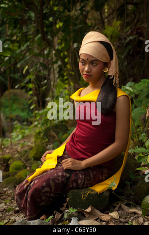 Traditionelle balinesische Tänzerin, die auf einem Felsen sitzt, während sie im Freien in einem Wald auftrat. Stockfoto