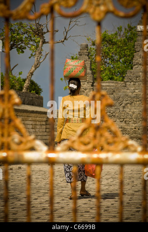 Rückansicht des balinesischen Frau, die religiöse Angebote zum Tempel in Korb auf dem Kopf trägt. Durch Tempel Tor geschossen. Stockfoto