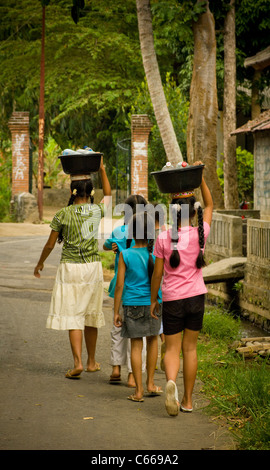 Rückansicht einer jungen asiatischen Frau und ihrer 3 Mädchen, die Schüsseln mit leeren Plastikflaschen auf ihren Köpfen trugen. Bali. Stockfoto