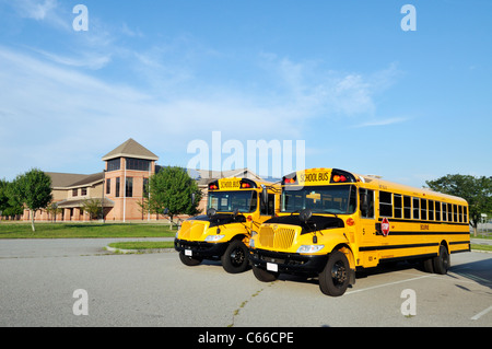 2 gelbe öffentliche Schulbusse geparkt nebeneinander auf Parkplatz außerhalb einer amerikanischen öffentlichen Schule USA. Stockfoto