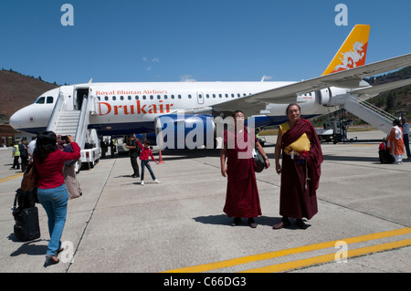Zwei Mönche und Touristen vor Drukair Flugzeug am Flughafen Paro. Bhutan Stockfoto