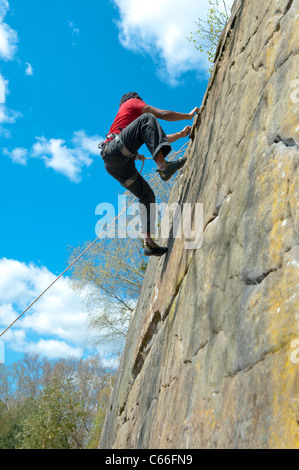Männliche Kletterer steigt eine in der Nähe von senkrechte Wand bei Harrisons Rocks in Kent, UK, wie er von seinem Partner unten gesichert ist. Stockfoto