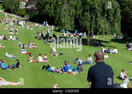 Ein Mann in der Princes Street Gardens Edinburgh sitzen am Menschen beim Sonnenbaden auf dem Gras wie ein Georges Seurat Malerei suchen Stockfoto