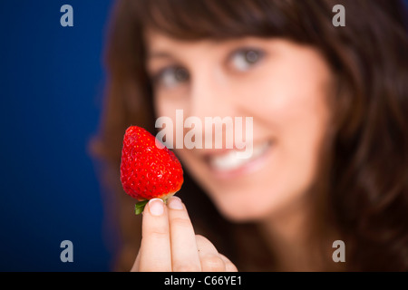 Schöne junge Frau halten und zeigen eine große und frische Erdbeere Stockfoto