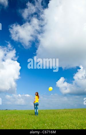 Glückliche junge Frau mit einem gelben Ballon auf der grünen Wiese Stockfoto