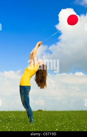 Glückliche junge Frau hält einen roten Ballon auf der grünen Wiese Stockfoto