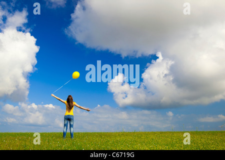 Glückliche junge Frau mit einem gelben Ballon auf der grünen Wiese Stockfoto