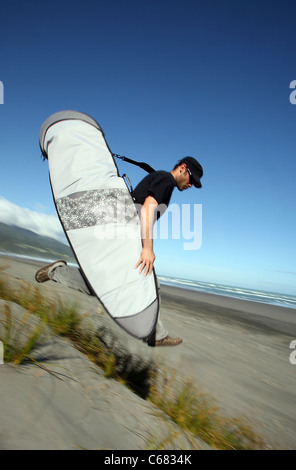 Junger Mann läuft die Sanddünen zum Surfen in Raglan, Neuseeland. Stockfoto