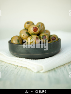 Grüne Oliven gefüllt mit Paprika mit Olivenöl und Kräutern in einem Topf Stockfoto