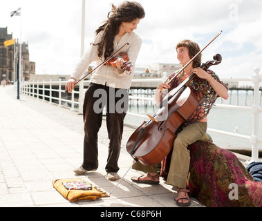 Zwei junge Leute spielen Cello und Violine als Straßenmusikant auf Aberystwyth promenade. Sommernachmittag Wales UK Stockfoto