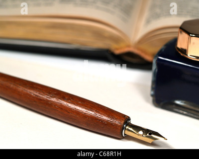 Detail-Foto eines alten Tintenfass und einen Stift, im Hintergrund ist ein aufgeschlagenes Buch Stockfoto