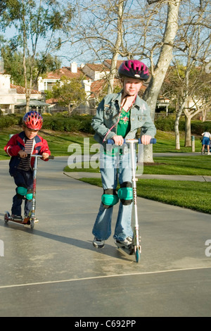 Tragen jacke Mädchen 6-7 Jahre alt und Pre-K Hispanic junge 4-5 Jahre alt auf Roller im Park. Herr © Myrleen Pearson Stockfoto