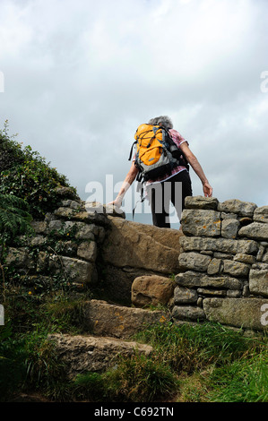 Rambler klettert über einen Stil auf dem Küstenpfad in Moelfre, Anglesey, Nordwales. Stockfoto